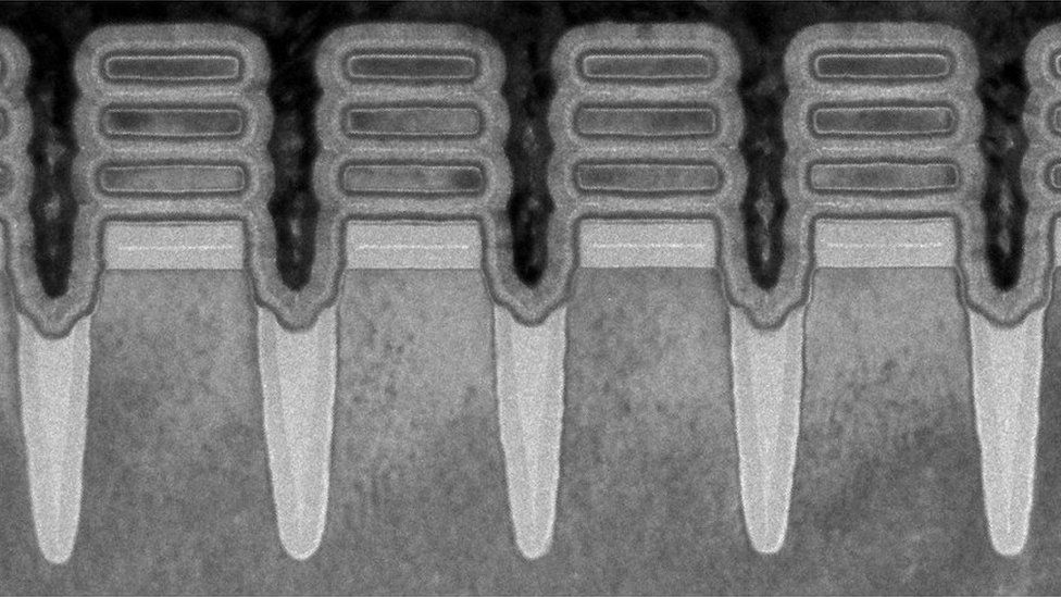 A microspcope image in black and white shows what appear to be four upright pillars with three floating "discs" at their top - a view of the transistors